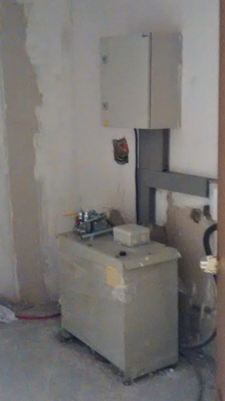 Gabinete eléctrico gris montado en pared con canaletas de cableado y unidad hidráulica en el suelo.