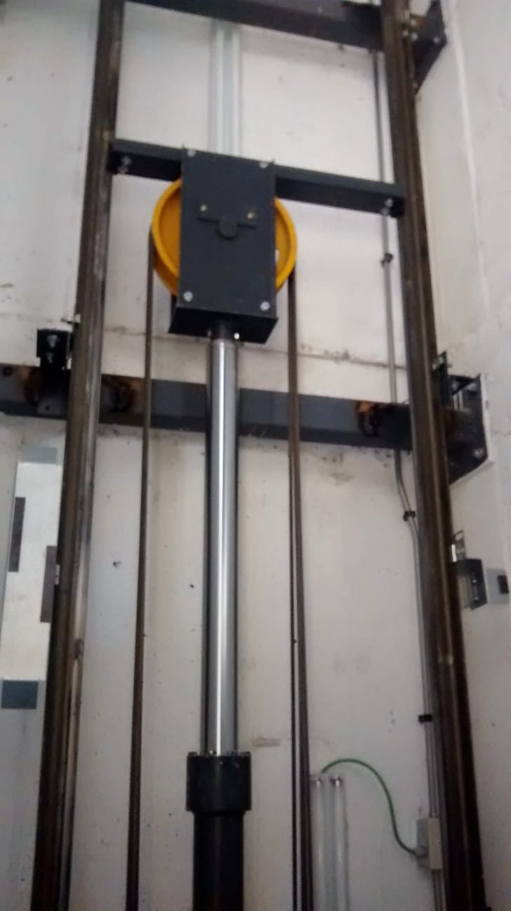 Sistema de poleas con pistón hidráulico cromado sosteniendo una polea amarilla por donde pasan los cables de tracción.